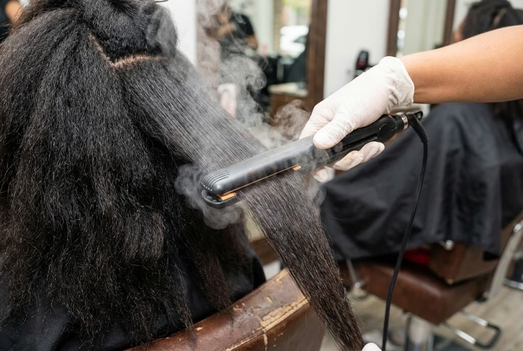 Plancha profesional alisando cabello con vapor en salón de belleza