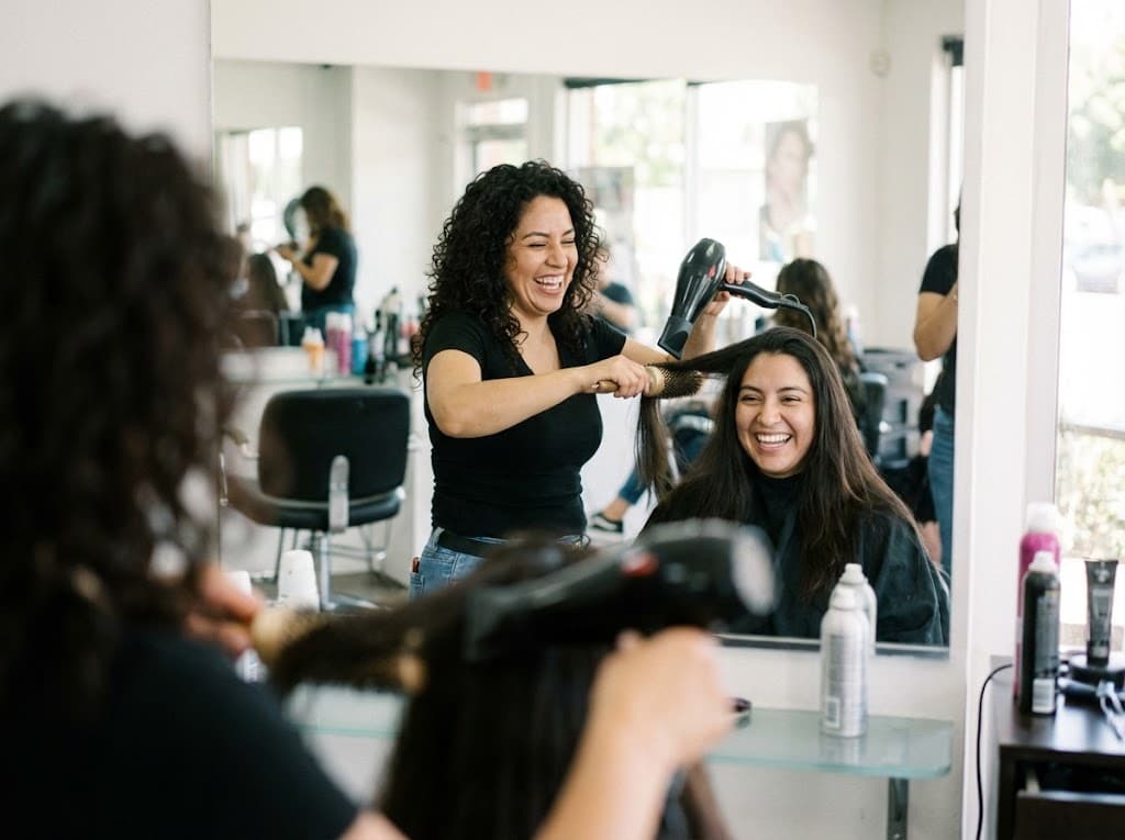 Estilista secando y peinando el cabello de clienta sonriente en salón
